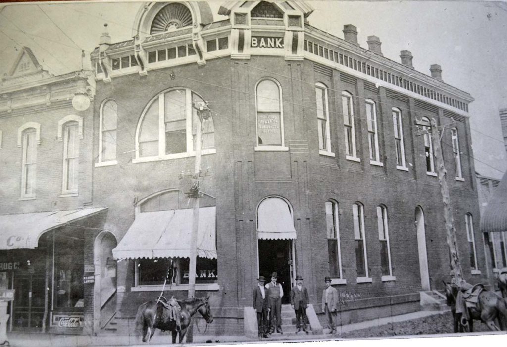 Old bank building in Van Alstyne with horses and people outside.